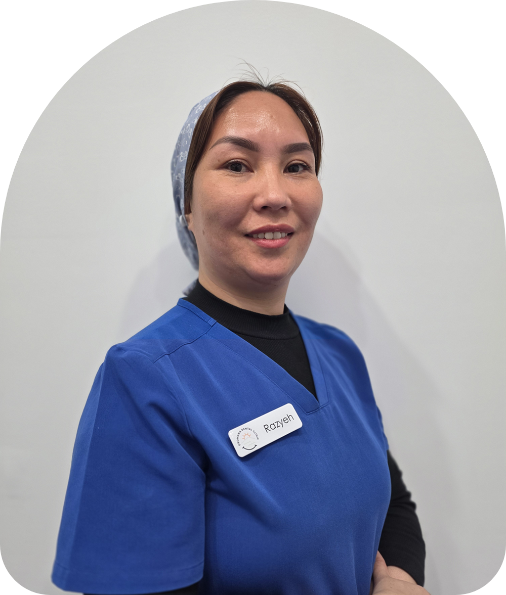 Portrait of a healthcare professional in blue scrubs smiling at the camera, wearing a light patterned cap and a name badge.